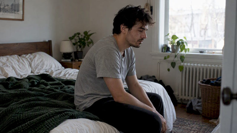 Tired adult sitting on bed in morning light